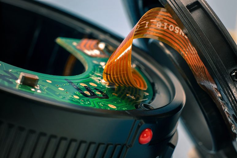 A green rigid circuit board with a polyimide flexible tail folded over it, inside a black housing